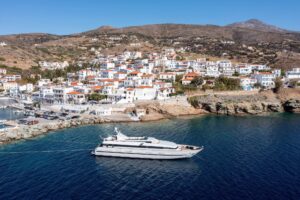 Andros island, Batsi village, Cyclades destination Greece. Aerial drone view of port, moored yacht, traditional building, clear sea water blue sky.