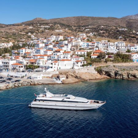 Andros island, Batsi village, Cyclades destination Greece. Aerial drone view of port, moored yacht, traditional building, clear sea water blue sky.