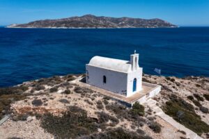 White small church at Kimolos island, Psathi port, aerial drone view. Rocky landscape, calm Aegean Sea, blue sky background. Greece Cyclades. Sunny windy day