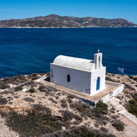 White small church at Kimolos island, Psathi port, aerial drone view. Rocky landscape, calm Aegean Sea, blue sky background. Greece Cyclades. Sunny windy day