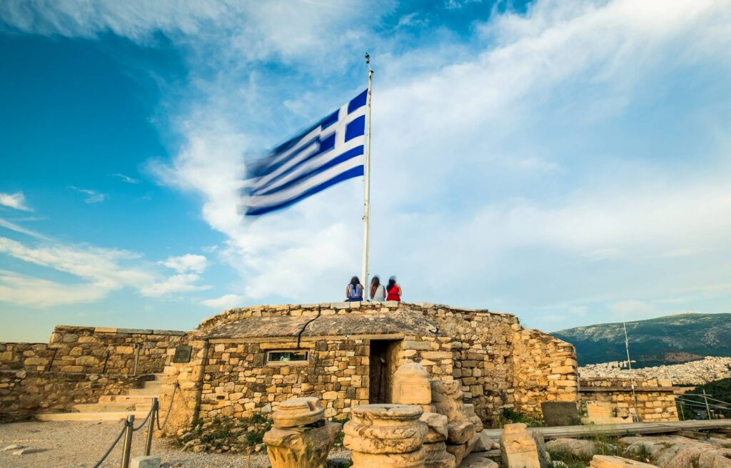 Greek national flag on flagpole waving against blue sky in Acropolis, Athens, Greece