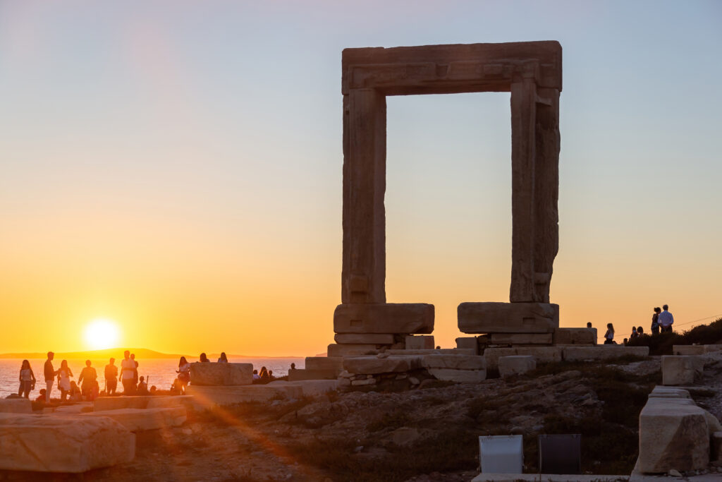 Naxos island, sunset over Temple of Apollo, Cyclades Greece. People admires the sundown from the islet of Palatia. Sunbeams paint the sky background.